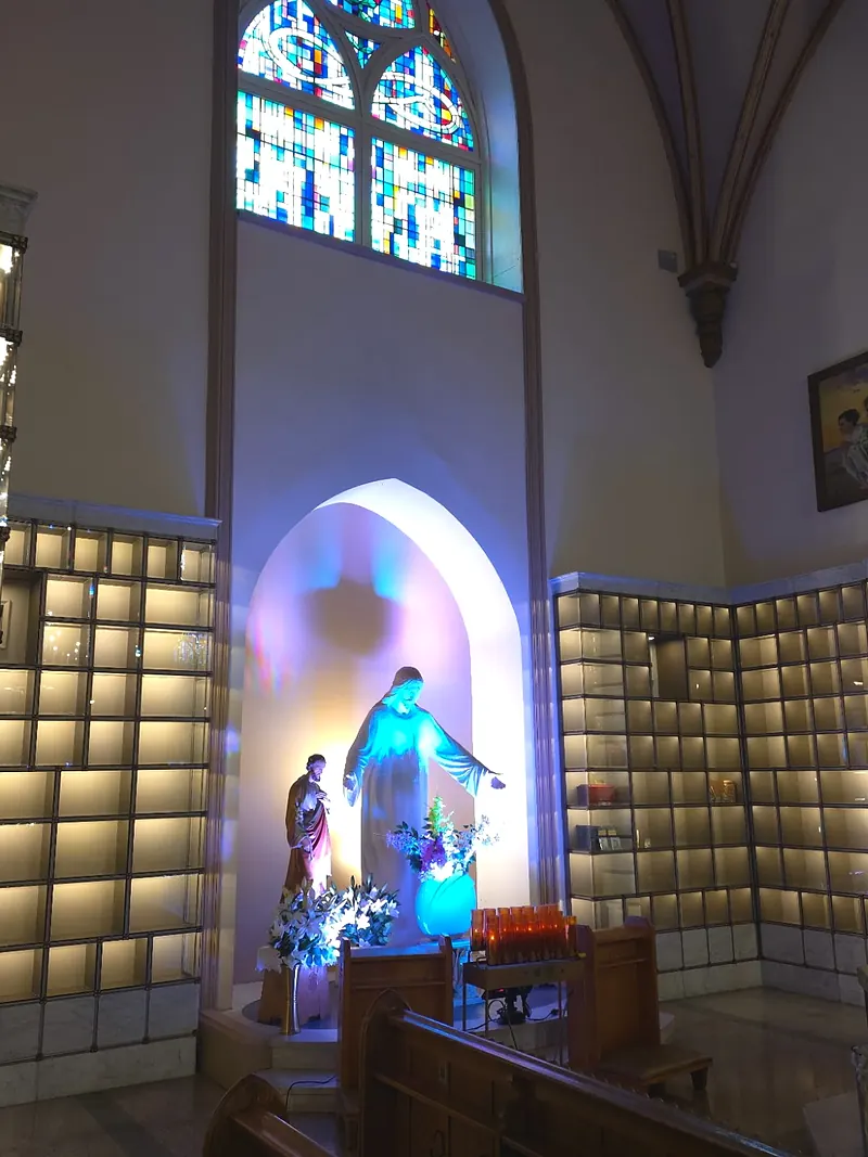 Tall pointed stained-glass window above the alcove with a statue of Christ, between two walls of glass niches.